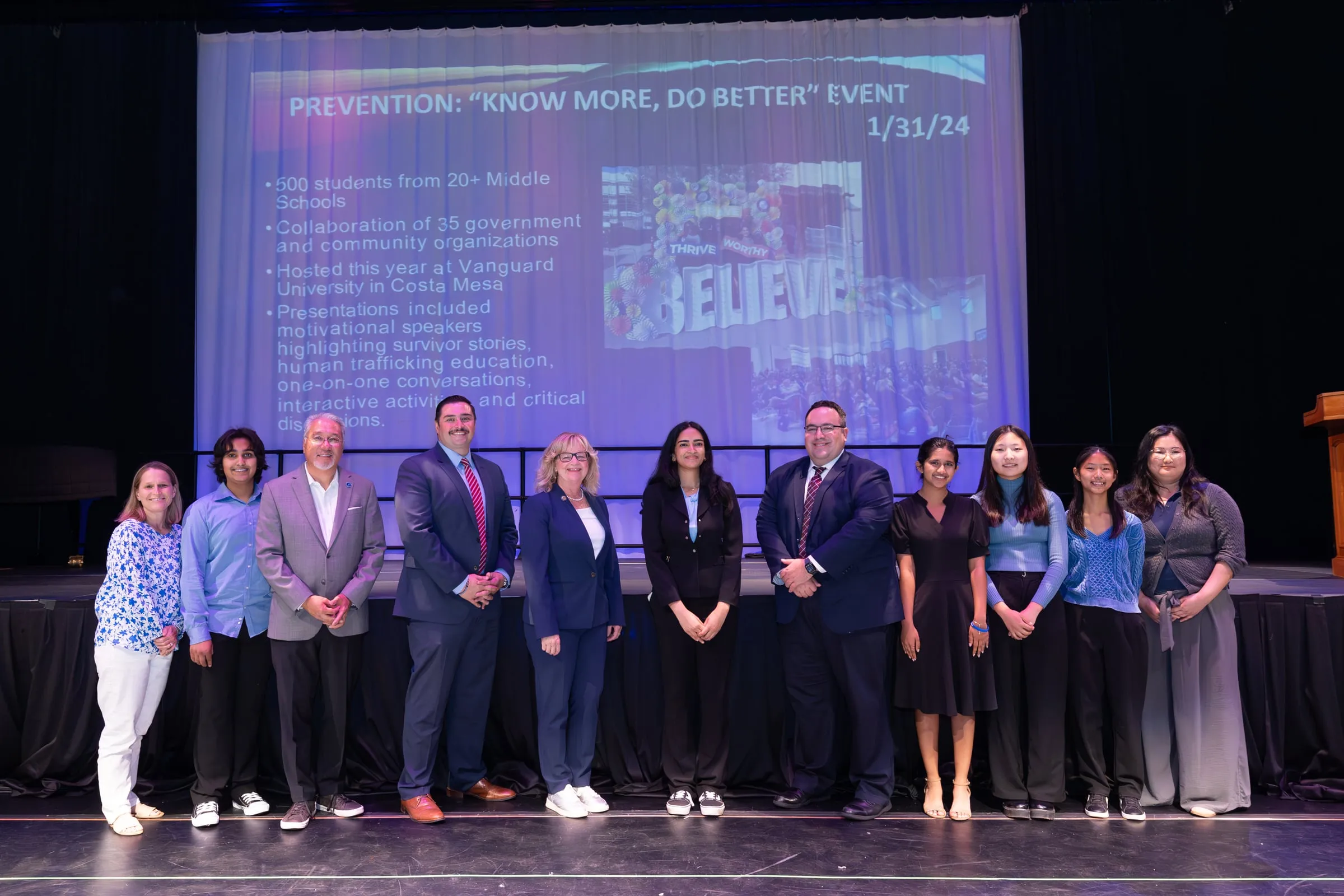 Eleven speakers and council members line up across the stage in front of a projected slide headed "Prevention: Know More, Do Better Event"