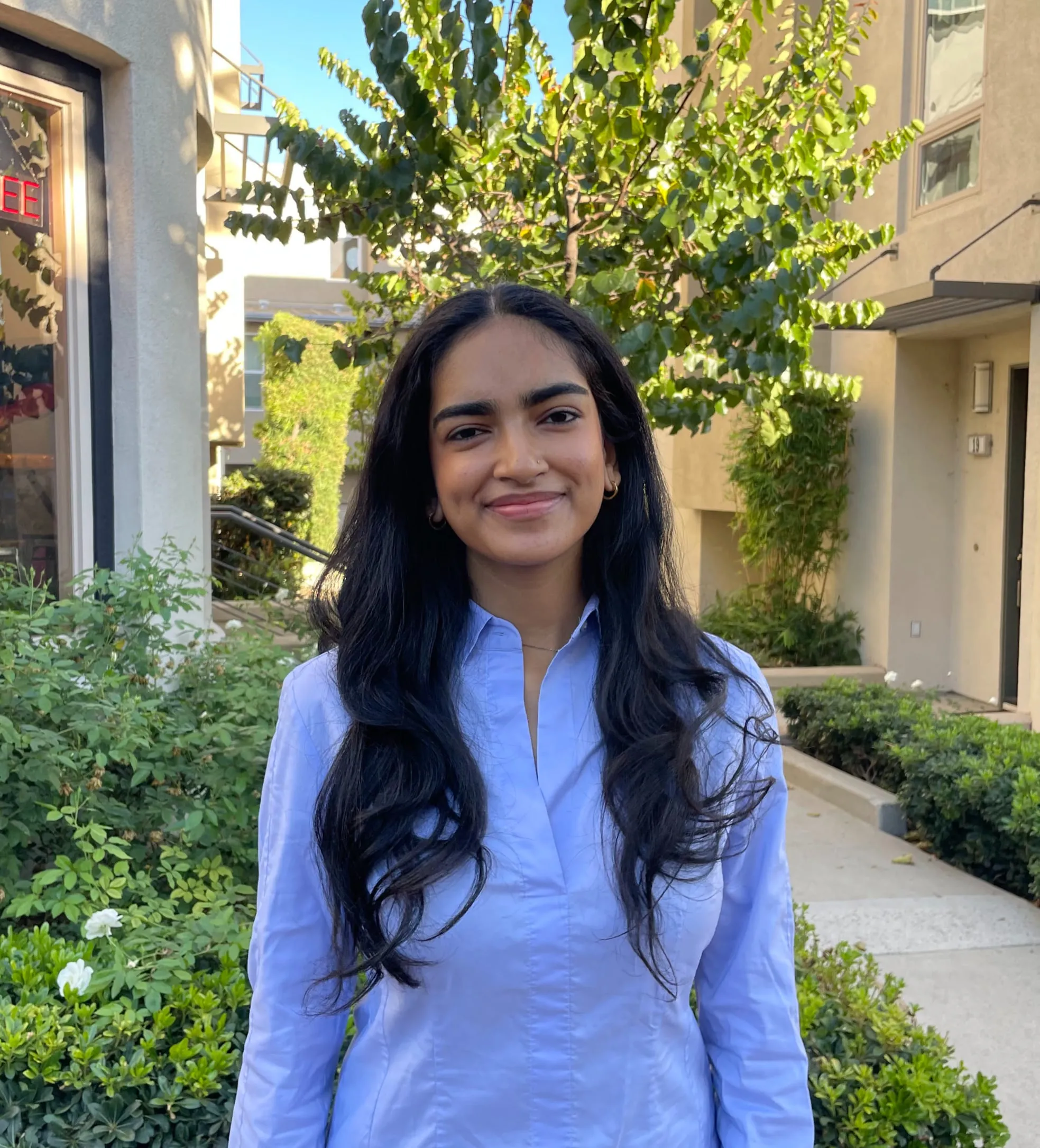 Sanvi Shah outdoors on a landscaped walkway, wearing a light blue button-up shirt